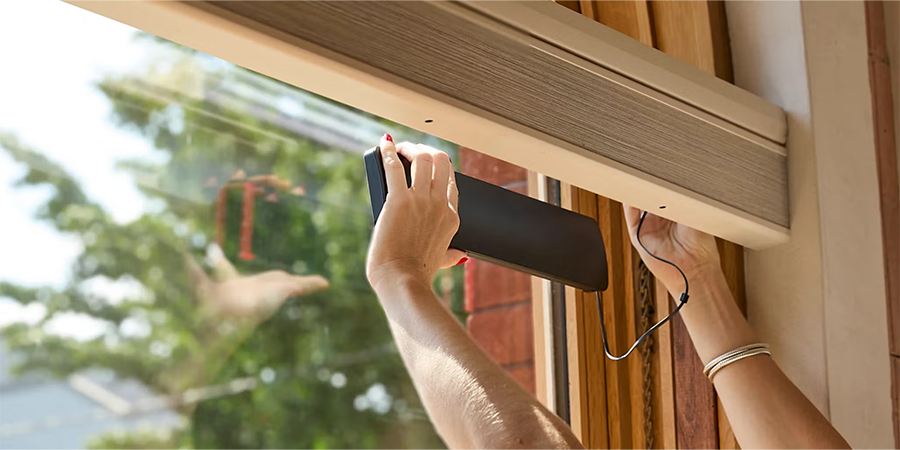 Hands installing PowerView solar charger connected to rechargeable battery wand with camel-colored shades