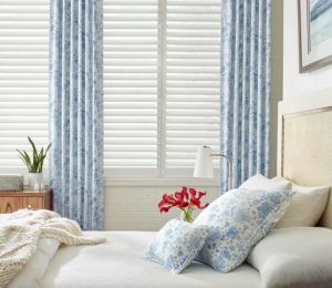 coastal guest bedroom white plantation shutters framed by blue floral curtains