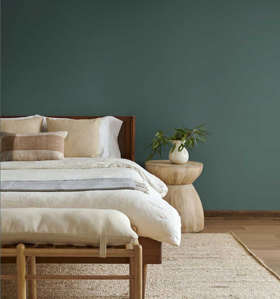 Teal green wall with a bed and nightstand pushed up against the wall