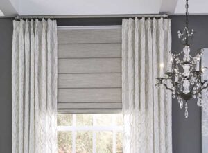 Pinch Pleat Drapery with Custom Roman Shade in a dark gray room with a nice chandelier