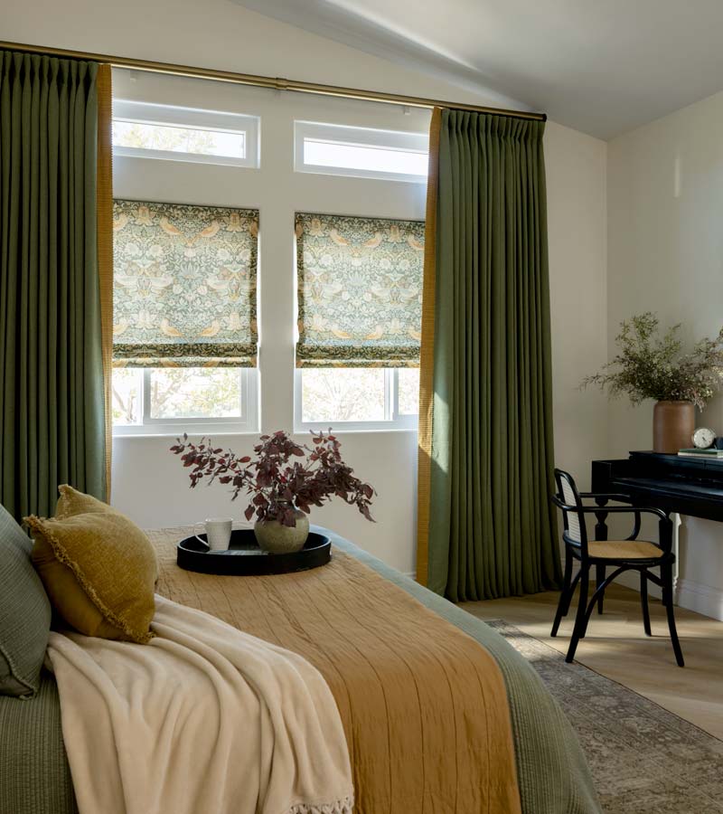 Green custom drapery panels on either side of two windows in a neutral toned bedroom 